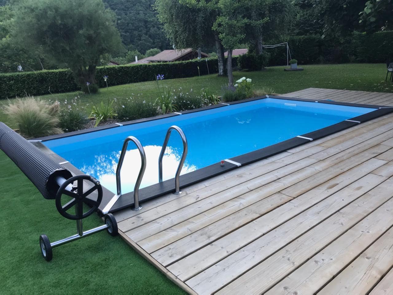 Piscine enterrée au bord d'une terrasse en bois au milieu d'un jardin